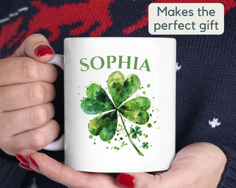 K&ouml;nnte beinhalten: Wei&szlig;e Keramiktasse mit einem gr&uuml;nen Aquarell-Kleeblatt-Design und dem Namen "SOPHIA" in Schwarz gedruckt.