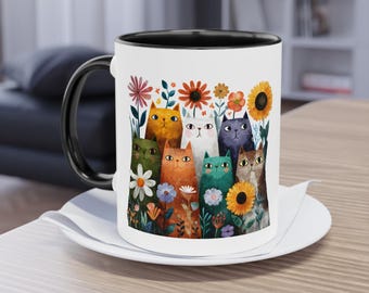 May include: A white ceramic mug with a black handle and interior, featuring a colorful illustration of various cats among flowers. The cats are in shades of orange, green, white, purple, and brown. The mug sits on a white saucer.