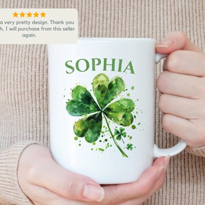 K&ouml;nnte beinhalten: Wei&szlig;e Keramiktasse mit einem gr&uuml;nen Aquarell-Kleeblatt-Design und dem Namen "SOPHIA" in Schwarz gedruckt.