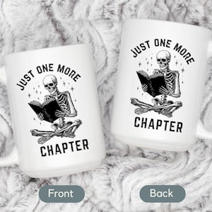 May include: Two white ceramic mugs with a black and white illustration of a skeleton reading a book. The text "JUST ONE MORE CHAPTER" is printed on the mugs. The mugs have a large handle.