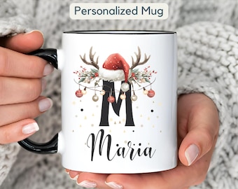 Könnte beinhalten: Weiße Keramik-Tasse mit schwarzem Henkel und Rand, mit einem Weihnachtsdesign. Das Design umfasst einen roten Weihnachtsmannhut, Geweih und den Buchstaben "M" mit dem Namen "Maria" darunter. Der Text "Personalized Mug" steht oben.