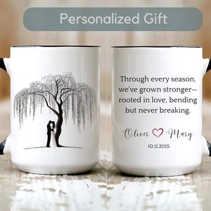 Puede incluir: Taza de cerámica blanca con asa y borde negros. Un lado presenta una ilustración en blanco y negro de una pareja bajo un sauce llorón. El otro lado tiene una cita y nombres con una fecha.