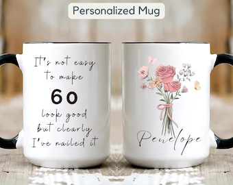 May include: White ceramic mug with a black handle and rim. One side has the text "It's not easy to make 60 look good but clearly I've nailed it." The other side features a floral design and the name "Penelope."
