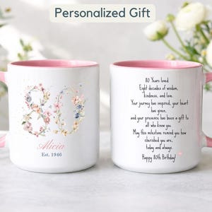 Puede incluir: Dos tazas de cerámica blanca con asas e interiores rosas. Una taza muestra el número 80 con flores, el nombre Alicia y Est. 1946. La otra taza tiene un poema sobre 80 años de vida, Happy 80th Birthday y un pequeño corazón rosa.