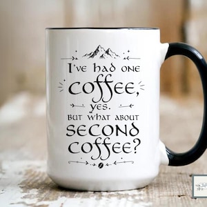 May include: White ceramic coffee mug with a black handle and rim. The mug features the text "I've had one coffee, yes. But what about second coffee?" in black script, along with a mountain illustration.