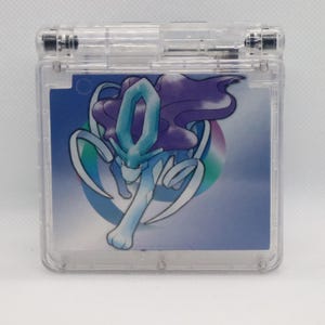Könnte beinhalten: Ein durchsichtiger Game Boy Advance SP aus Plastik mit einem blauen und violetten Pokémon-Charakter auf dem Bildschirm. Der Charakter ist eine blaue und weiße Kreatur mit langen, fließenden Haaren und einem großen, blauen Edelstein auf dem Kopf.
