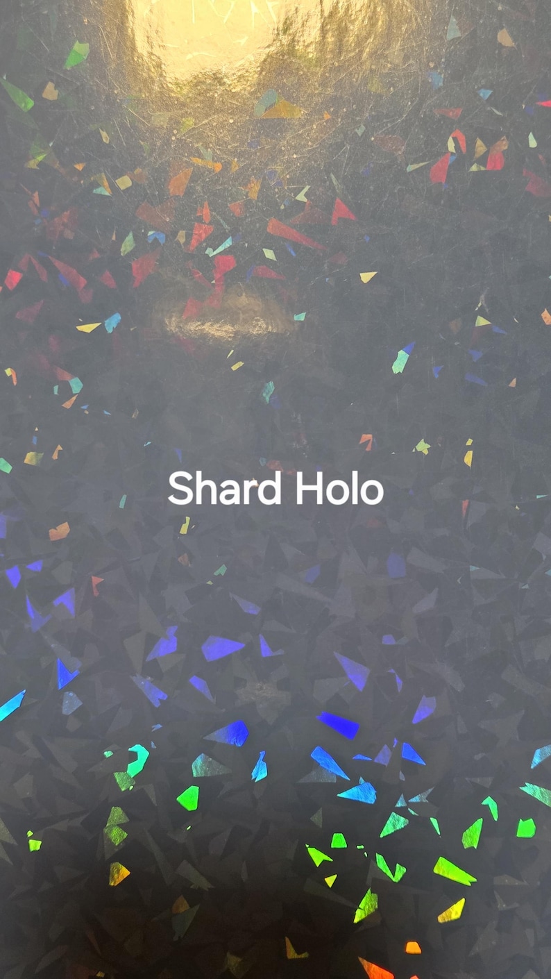Puede incluir: Una superficie gris oscuro con un patr&oacute;n hologr&aacute;fico de fragmentos. La superficie est&aacute; cubierta de peque&ntilde;as formas irregulares que reflejan m&uacute;ltiples colores, incluyendo azul, verde y naranja. El texto "Shard Holo" est&aacute; impreso en blanco.