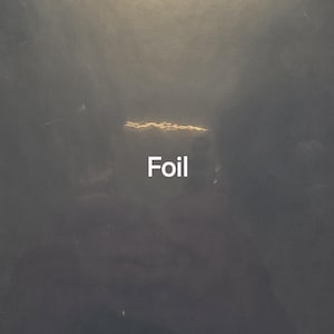 Puede incluir: Una superficie oscura y texturizada con una fuente de luz circular y brillante en la parte superior. La palabra "Foil" se muestra en texto blanco. La imagen tiene una apariencia nublada y atmosf&eacute;rica.