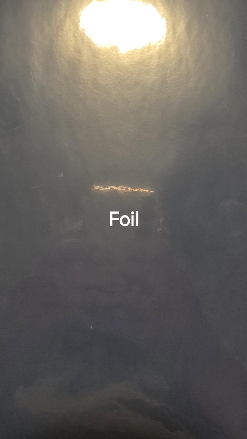Puede incluir: Una superficie oscura y texturizada con una fuente de luz circular y brillante en la parte superior. La palabra "Foil" se muestra en texto blanco. La imagen tiene una apariencia nublada y atmosf&eacute;rica.