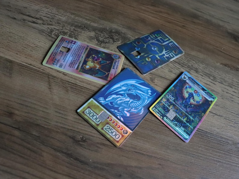 Puede incluir: Cuatro cartas coleccionables de juegos de cartas, incluyendo una carta de Charizard y una carta de Drag&oacute;n Blanco de Ojos Azules. Las cartas son rectangulares con varios dise&ntilde;os y textos coloridos, sobre una superficie de madera.