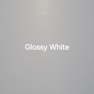 Puede incluir: Primer plano de una superficie blanca brillante. Las palabras "Glossy White" est&aacute;n centradas en la superficie en una fuente blanca sans-serif. El fondo es un degradado de blanco y gris.
