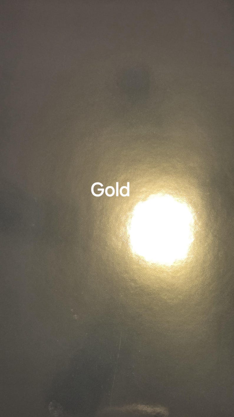Puede incluir: Superficie oscura y texturizada con la palabra "Gold" en letras blancas. Una luz dorada brillante emana del centro, creando un efecto de foco. La est&eacute;tica general es minimalista y elegante.