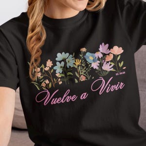 May include: Black t-shirt featuring a floral design and the text "Vuelve a Vivir" in pink. The text "EZ. 36:26" is also visible on the shirt.