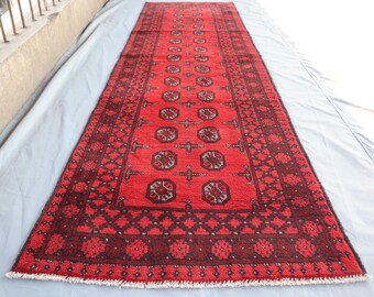 May include: A red runner rug with a traditional Persian design. The rug has a dark red background with a black and white geometric pattern. The rug has a fringe border.