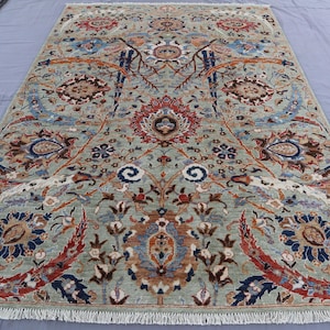 May include: A rectangular rug featuring a light green backdrop and a complex floral design in red, blue, brown, and cream. The rug has a fringed border and a detailed, symmetrical pattern, ideal for home decoration.
