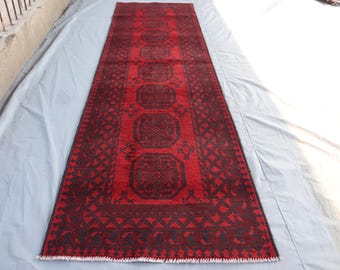 May include: A red and black runner rug with a traditional Persian design. The rug has a fringed edge and is made of wool.