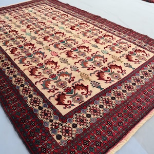 May include: A cream-colored rug with a red, green, and blue floral pattern. The rug has a detailed border with intricate designs.