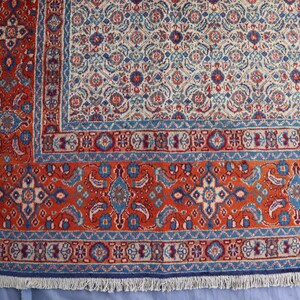 May include: A rectangular area rug featuring a dense, intricate floral and geometric pattern in shades of deep red, cream, and blue. The design includes a wide, ornate border with repeating motifs and a central field with a repeating pattern.