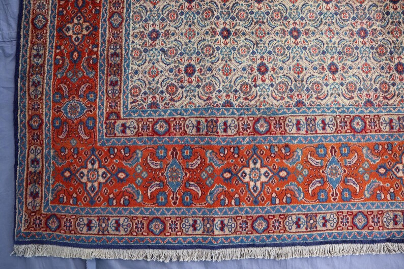 May include: A rectangular area rug featuring a dense, intricate floral and geometric pattern in shades of deep red, cream, and blue. The design includes a wide, ornate border with repeating motifs and a central field with a repeating pattern.