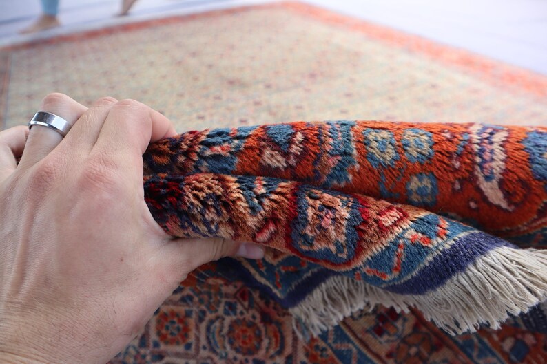 May include: A rectangular area rug featuring a dense pile with a complex pattern in shades of rust orange, deep blue, and cream. The rug has a visible fringe along the edge and a thick, textured weave that shows intricate floral and geometric motifs.
