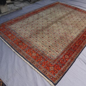 May include: A rectangular area rug featuring a cream-colored central field densely covered in a repeating floral pattern, framed by a wide, vibrant red border with intricate geometric and botanical motifs, finished with short white fringe at ends.