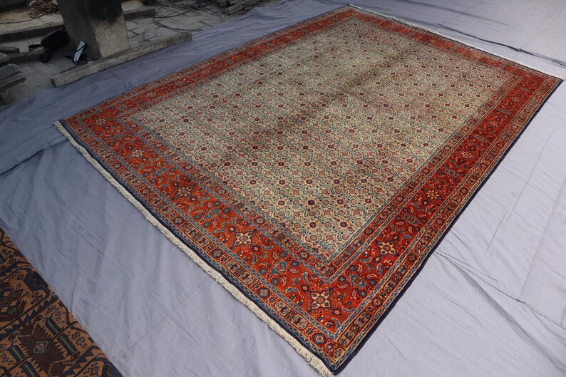 May include: A rectangular area rug featuring a cream-colored central field densely covered in a repeating floral pattern, framed by a wide, vibrant red border with intricate geometric and botanical motifs, finished with short white fringe at ends.