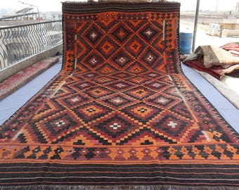 May include: A large, rectangular rug with a geometric diamond pattern in shades of orange, brown, and black. The rug has a fringed edge and is displayed outdoors. The design features repeating diamond shapes with white and black accents.