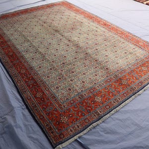 May include: A rectangular area rug featuring a central field of cream with an intricate all-over floral pattern in shades of blue, red, and tan. The rug is framed by a wide, vibrant red border decorated with detailed floral motifs and blue accents.