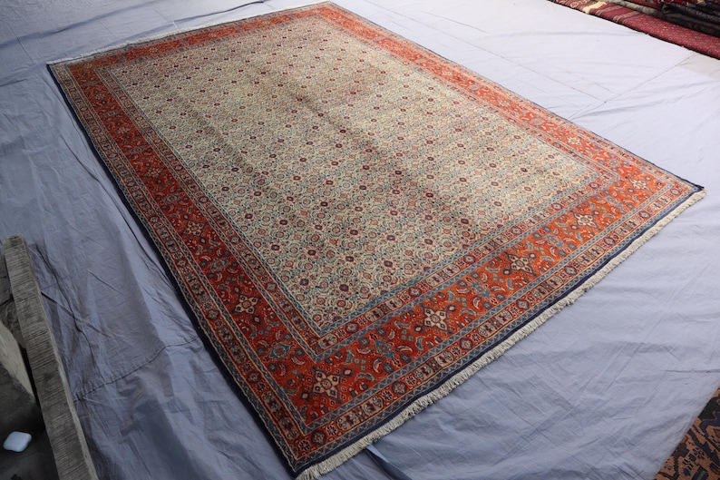 May include: A rectangular area rug featuring a central field of cream with an intricate all-over floral pattern in shades of blue, red, and tan. The rug is framed by a wide, vibrant red border decorated with detailed floral motifs and blue accents.
