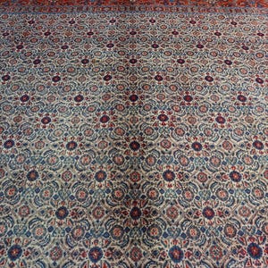May include: A large rectangular area rug featuring an intricate repeating floral and geometric pattern in shades of cream, deep red, navy blue, and muted teal. The design consists of small circular medallions surrounded by dense botanical motifs.