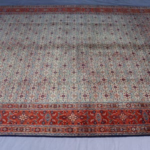 May include: A large rectangular area rug featuring a central field of cream, light blue, and dark red intricate floral patterns. The rug is framed by a wide, bold border in deep red with repeating geometric and floral motifs in blue and cream.