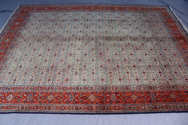 May include: A large rectangular area rug featuring a central field of cream, light blue, and dark red intricate floral patterns. The rug is framed by a wide, bold border in deep red with repeating geometric and floral motifs in blue and cream.