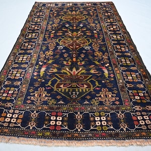 May include: A rectangular area rug featuring a deep navy blue background with a central urn motif and symmetrical floral patterns in shades of red, green, and cream. The rug has a detailed border and light-coloured fringe on both ends.