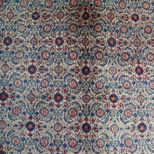 May include: A textile featuring a repeating geometric pattern in shades of deep blue, muted red, and cream. The design consists of interconnected floral-like medallions and intricate scrollwork arranged in a dense, symmetrical grid across the surface.