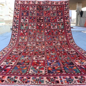 May include: A traditional Persian rug with a geometric pattern in shades of red, blue, and white. The rug is made of wool and has a fringed border.