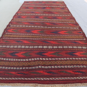 May include: A red, brown and blue patterned rug with a geometric design. The rug has a fringed border.