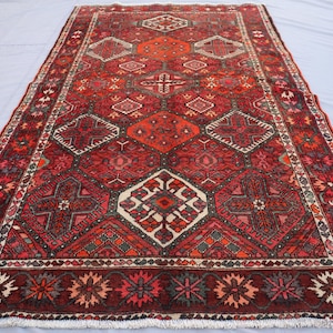 May include: A rectangular, hand-knotted rug with a rich, red colour palette. The rug features intricate geometric patterns in shades of red, orange, and cream. The border has a floral design. The rug is likely made of wool.