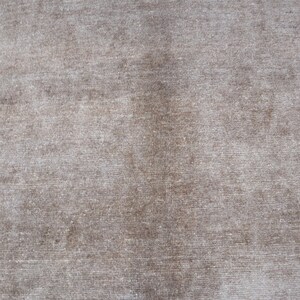 May include: A close-up shot of a textured, neutral-toned fabric. The material has a soft, velvety appearance with subtle variations in color, creating a sense of depth and dimension. The fabric's surface is slightly uneven.