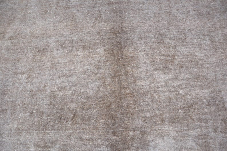 May include: A close-up shot of a textured, neutral-toned fabric. The material has a soft, velvety appearance with subtle variations in color, creating a sense of depth and dimension. The fabric's surface is slightly uneven.