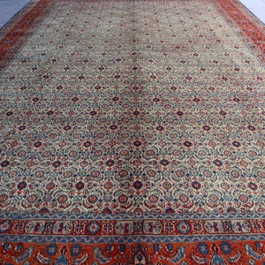 May include: A large rectangular area rug featuring an intricate all-over floral pattern in shades of cream, deep red, and navy blue. The central field is surrounded by a wide, ornate border in vibrant red with blue and cream decorative motifs.