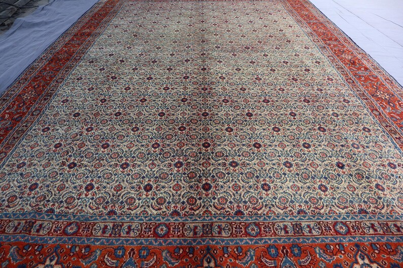 May include: A large rectangular area rug featuring an intricate all-over floral pattern in shades of cream, deep red, and navy blue. The central field is surrounded by a wide, ornate border in vibrant red with blue and cream decorative motifs.