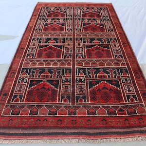 May include: A red, black and cream rug with a geometric pattern. The rug has a fringed border.