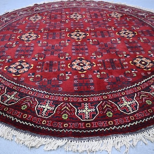 May include: A round, red rug with an intricate geometric pattern. The rug features a central design with repeating shapes in shades of black, yellow, and white. The border has a detailed pattern with a fringe.