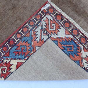 May include: A brown rug with a detailed border featuring red, blue, and cream geometric patterns. The rug's design is visible on the corner, showcasing the intricate craftsmanship and color palette.