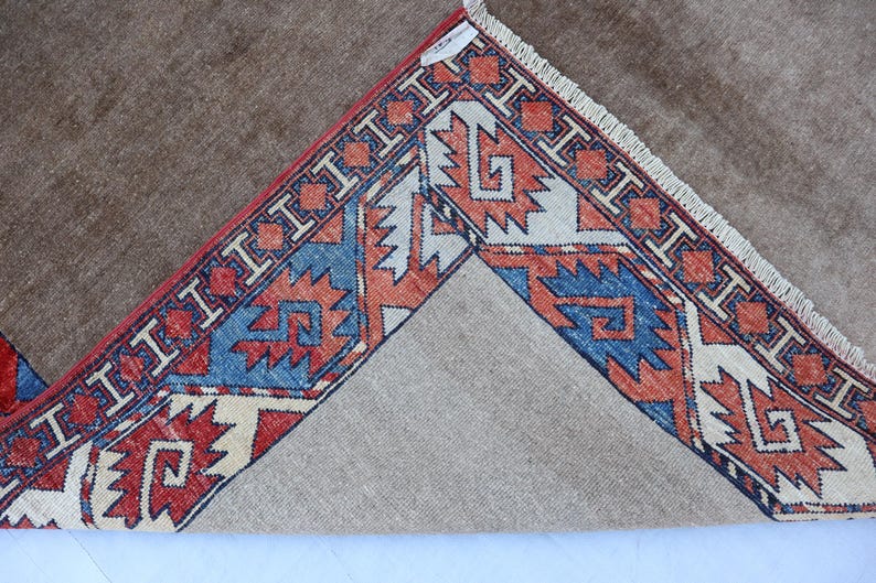 May include: A brown rug with a detailed border featuring red, blue, and cream geometric patterns. The rug's design is visible on the corner, showcasing the intricate craftsmanship and color palette.