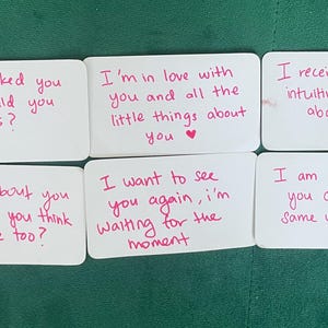Op de afbeelding: Zes rechthoekige witte kaarten met afgeronde hoeken, elk voorzien van handgeschreven roze tekst. De berichten zijn: If I asked you out, would you say yes?, I'm in love with you and all the little things about you, I receive psychic/intuitive messages about you, I think about you a lot! Do you think about me too?, I want to see you again, i'm waiting for the moment, en I am scared that you don't feel the same way.