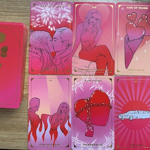 Puede incluir: Una baraja de cartas de tarot rosa y dorada con ilustraciones. Las cartas presentan imágenes de parejas, corazones y una limusina. La baraja incluye cartas con las etiquetas "Age of Fluted", "First Date", "The Hot Seat" y "Possessive".