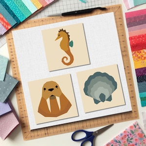 May include: Three square art prints depicting marine life: a seahorse, a walrus, and a scallop shell. The seahorse is orange and brown, the walrus is brown, and the shell is grey. The prints are on a cream background.