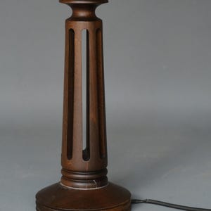 Könnte beinhalten: Eine dunkelbraune Tischlampe aus Holz mit einem zylindrischen Sockel und einem geschnitzten Design. Die Lampe hat ein schlichtes, elegantes Design.