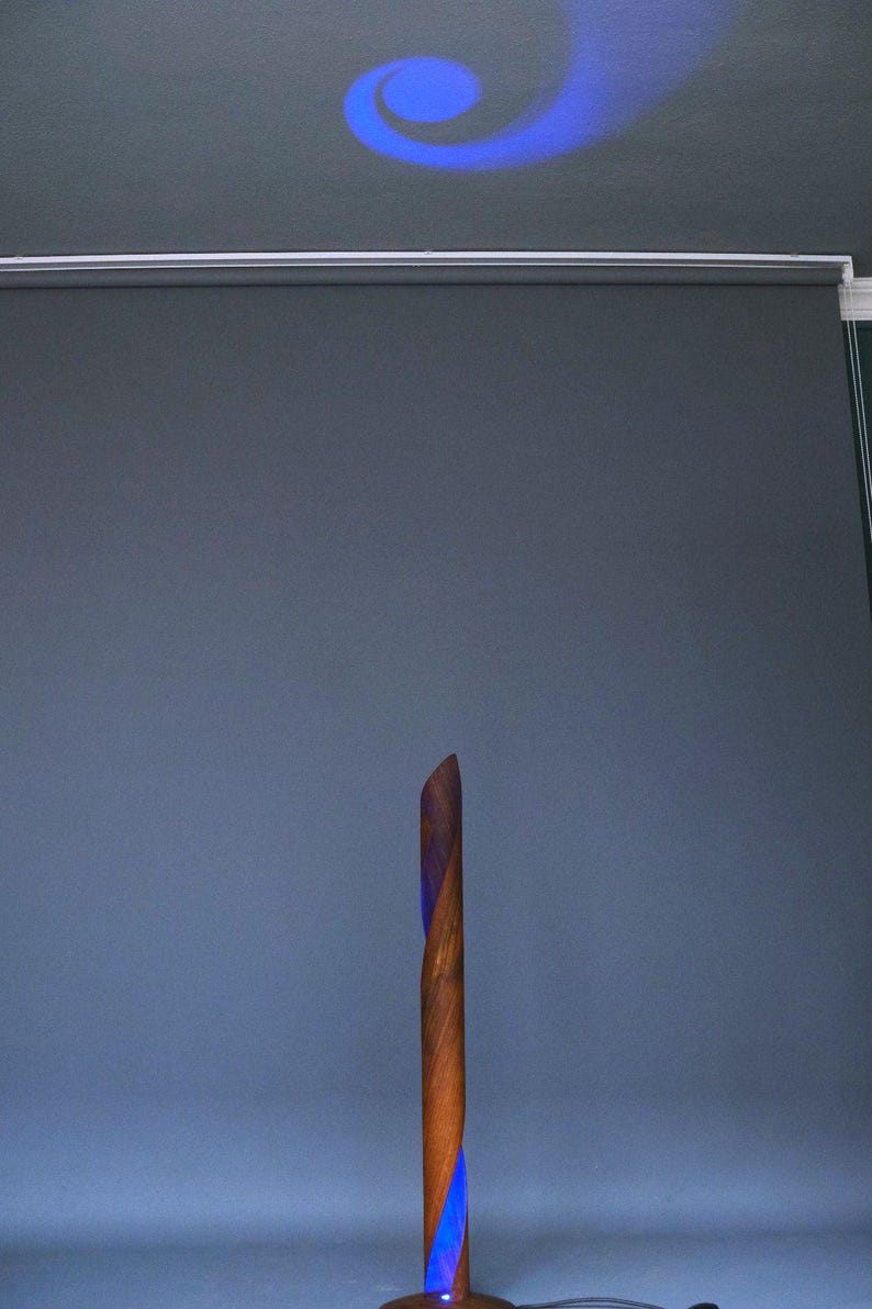 A wooden lamp with a blue light shining through the center. The lamp is made of a twisted piece of wood and has a dark brown finish.